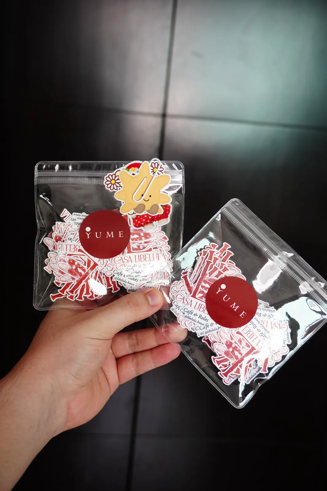 Dos bolsitas transparentes con stickers del logo de un negocio y el sello de Yume, sostenidas en la mano